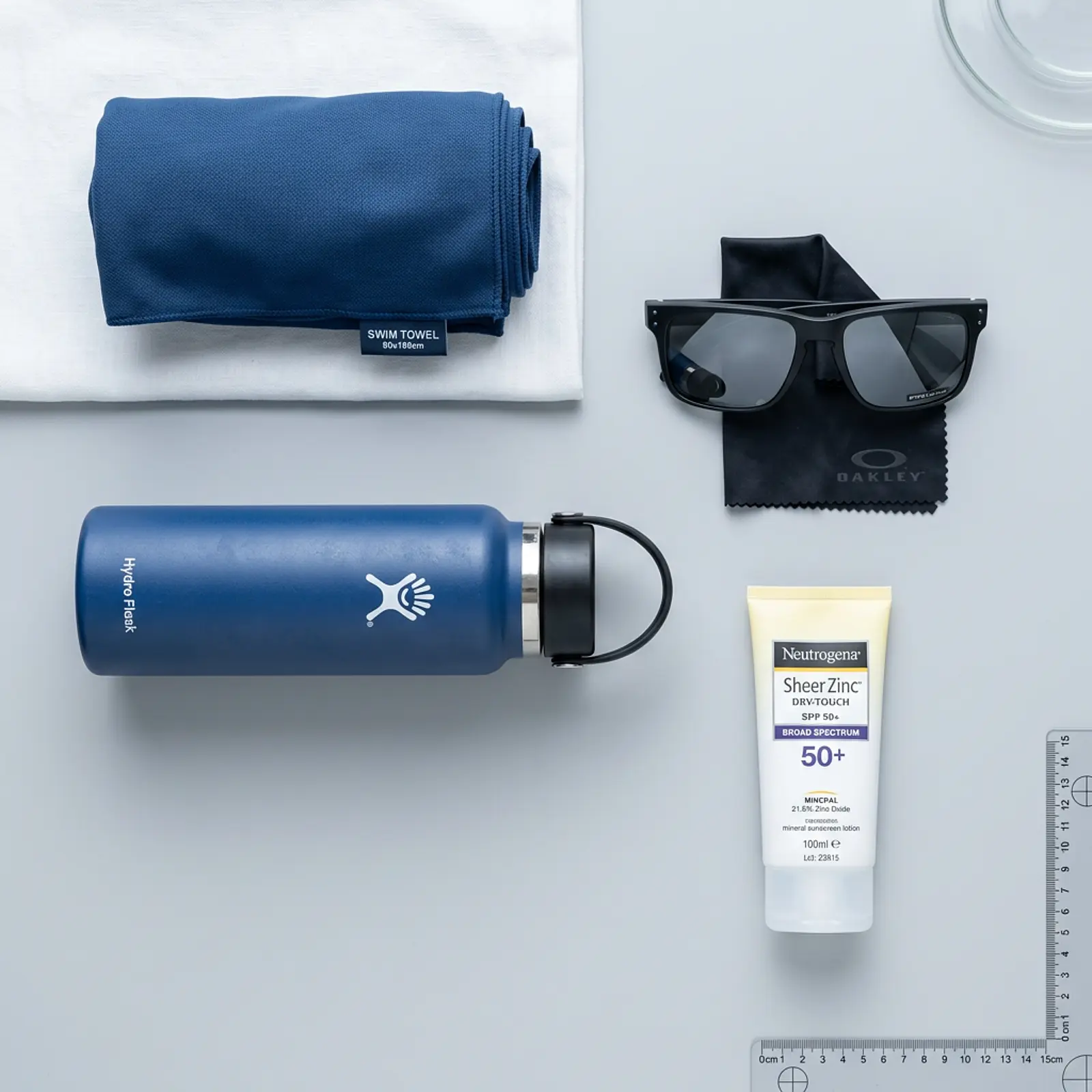 Studio flat lay: sunscreen, beach towel, sunglasses, and water bottle.