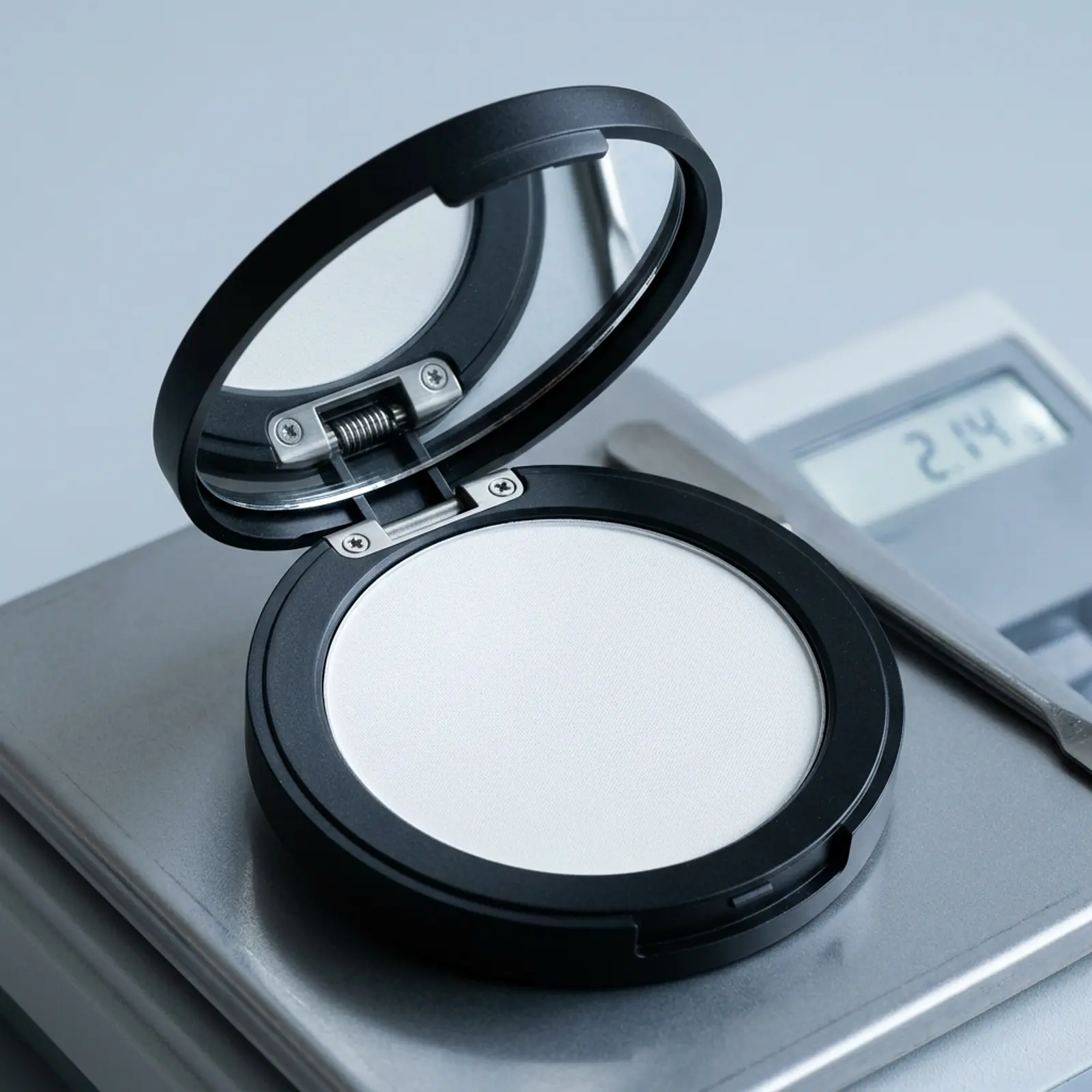 Open makeup compact revealing pristine white powder in a clean studio with cool daylight.