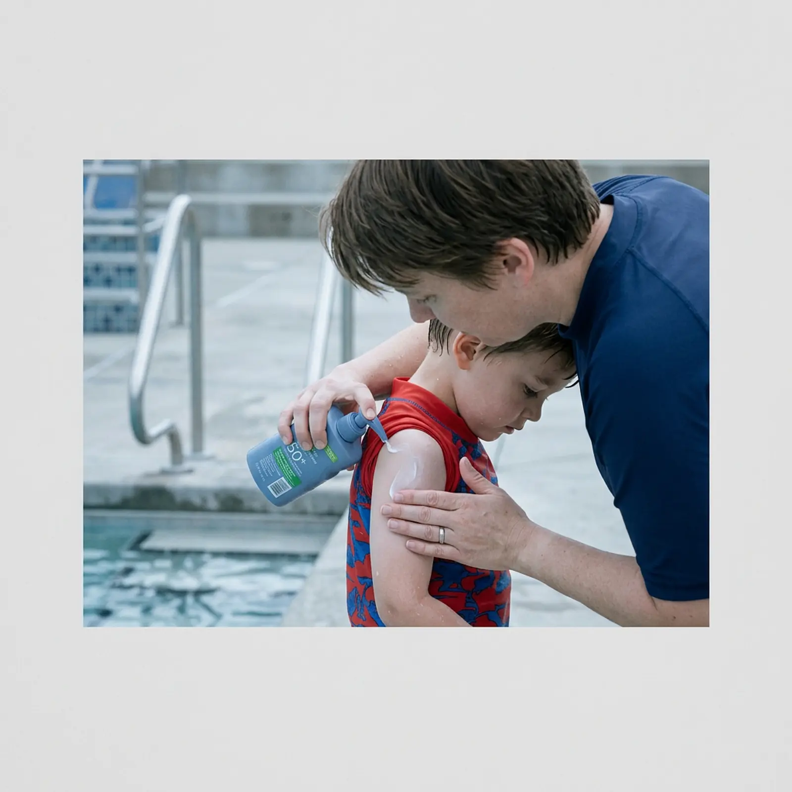 Parent applying sunscreen to a child's shoulders at an outdoor pool.